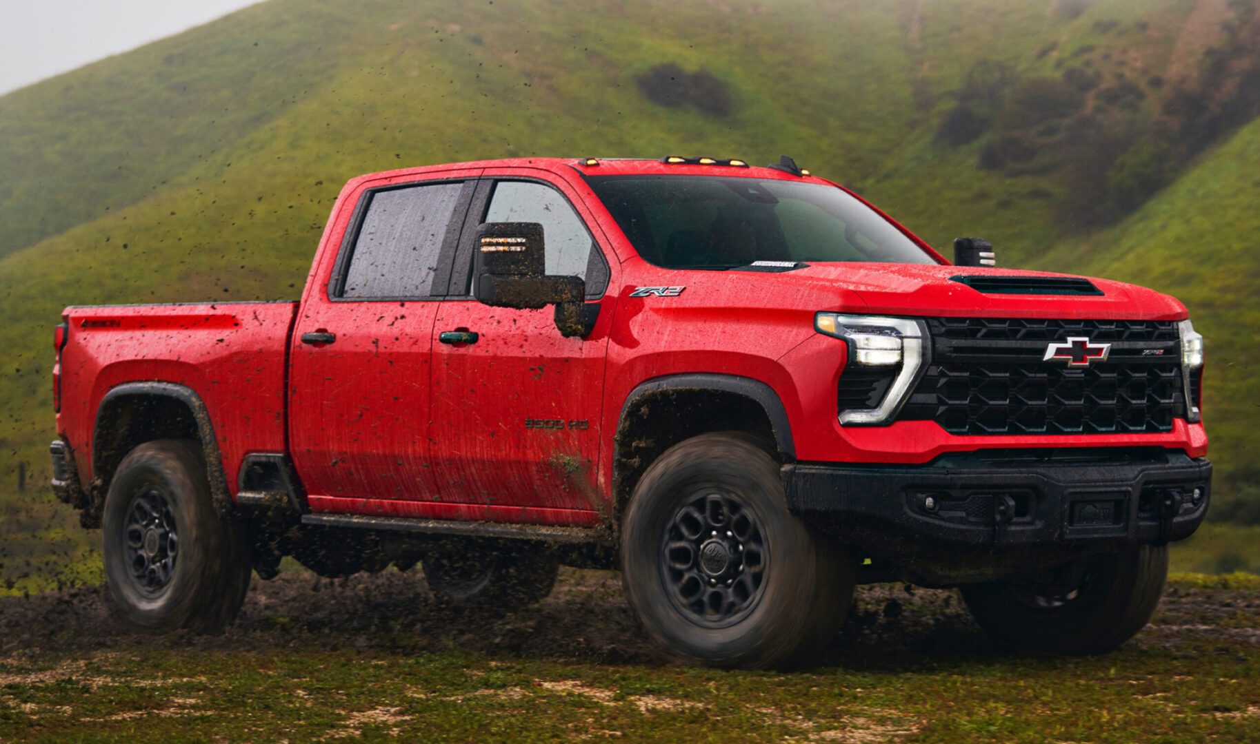 The red 2020 chevrolet silverado is driving through a muddy field.